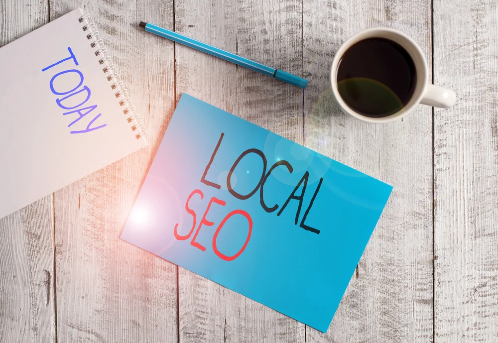 Writing note showing Local Seo. Business photo showcasing helps businesses promote products and services to local customers Stationary placed next to a cup of black coffee above the wooden table.